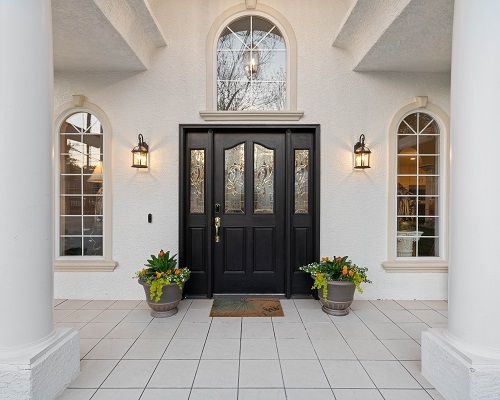 A stylish front entryway with a black door, arched windows, and decorative planters.