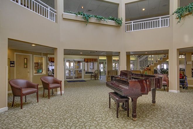 A spacious lobby area featuring a grand piano and comfortable seating, with balconies and indoor plants enhancing the decor.