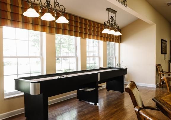 A well-lit game room featuring a sleek shuffleboard table and elegant chandeliers.