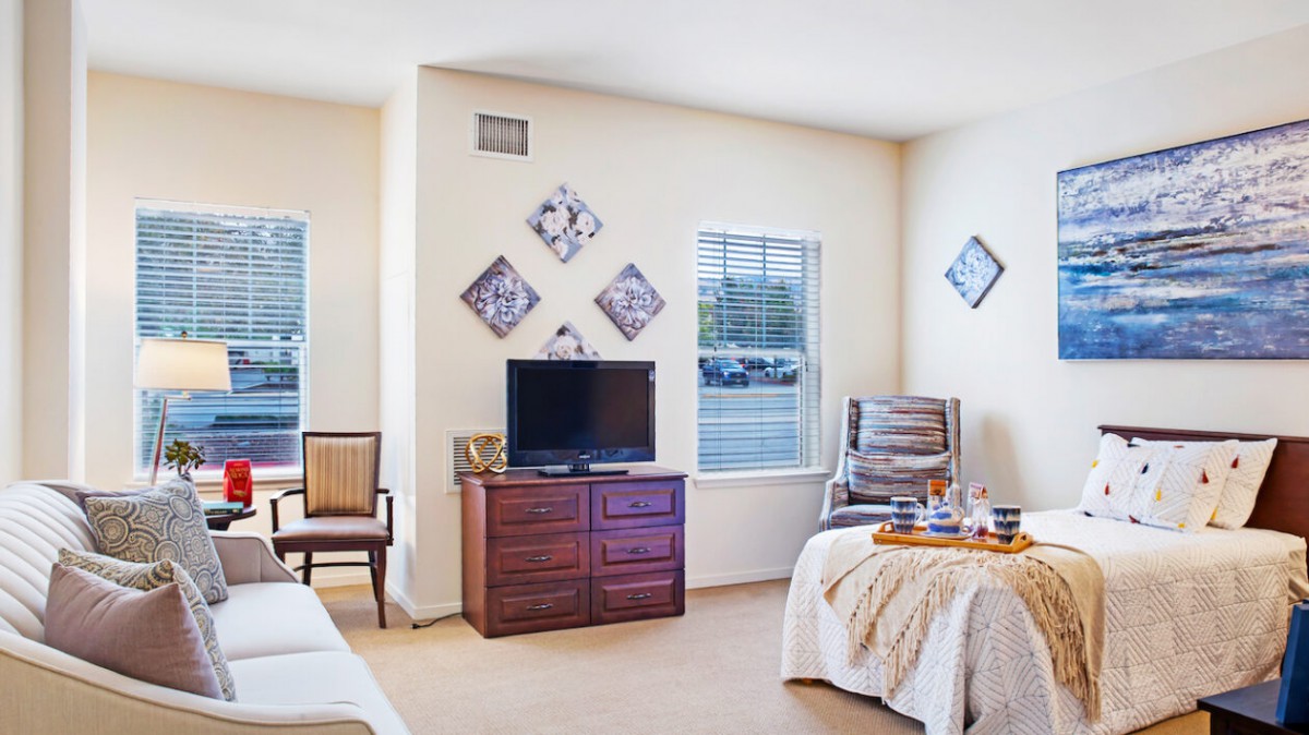 A bright and cozy living room with a television, comfortable chairs, and decorative wall art.