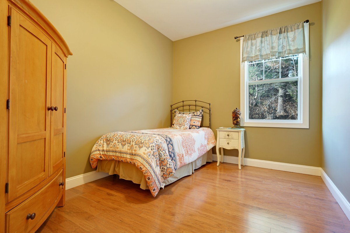 A cozy single bedroom with wooden flooring and simple furnishings.