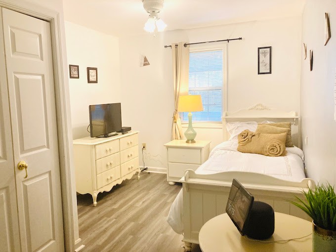 A cozy bedroom featuring a bed, TV, and nightstand with a lamp, complemented by wooden flooring and bright decor.