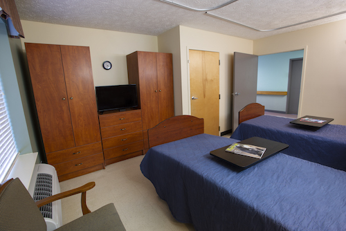 A spacious hospital room featuring two beds, wooden furniture, and a television.