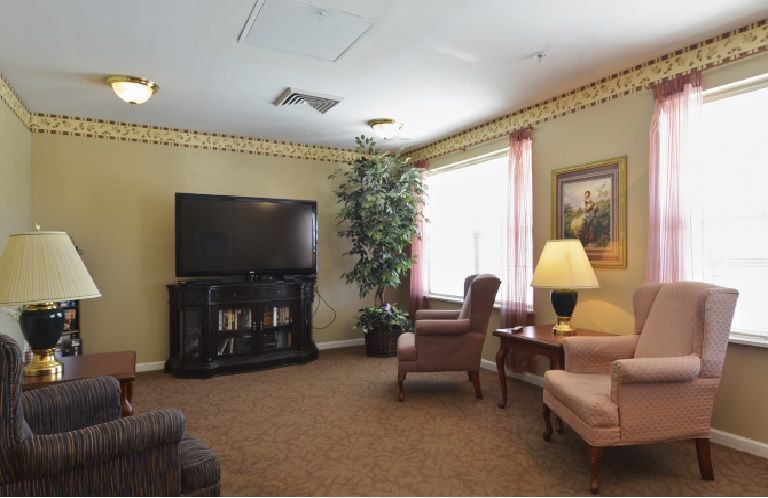 A cozy living room with a television, armchairs, and a lamp.