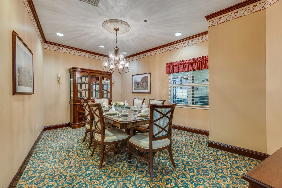 An elegant dining room featuring a chandelier, dining table with chairs, and a china cabinet on a patterned carpet.
