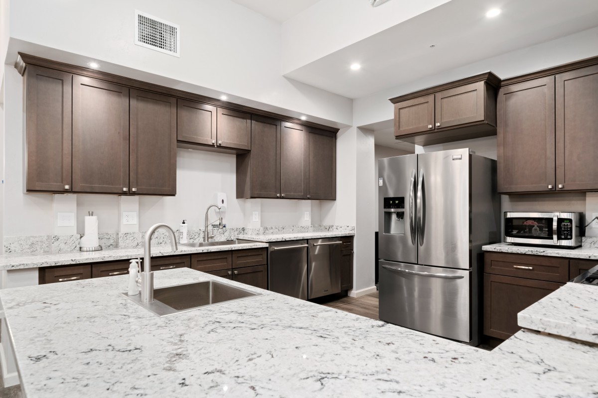 A modern kitchen with dark cabinets, stainless steel appliances, and a marble countertop.