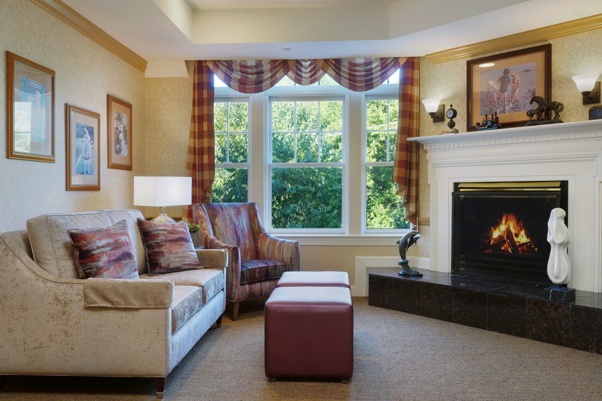 A cozy living room with a sofa, armchair, and fireplace, adorned with tasteful decor and a large window letting in natural light.