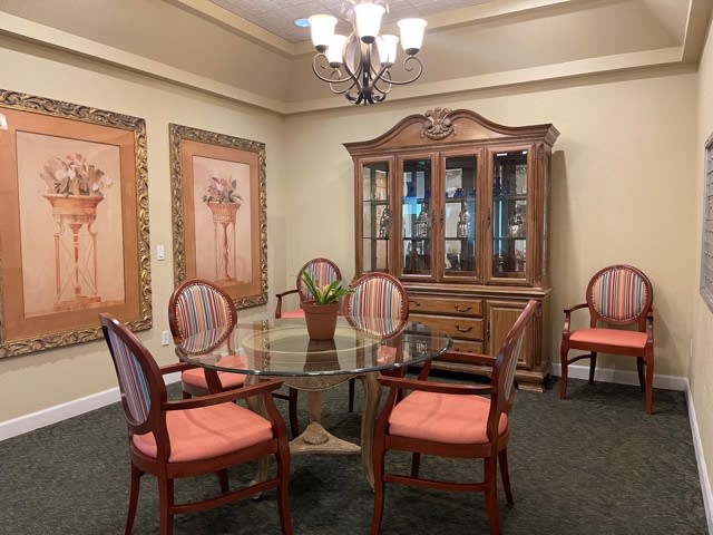 A traditional dining room with a glass table, upholstered chairs, and a decorative cabinet.