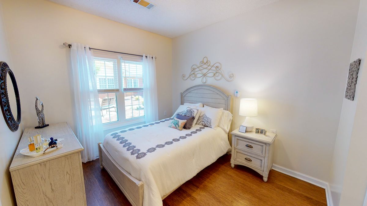 A cozy bedroom with a neatly made bed, nightstand, and lamp by the window.