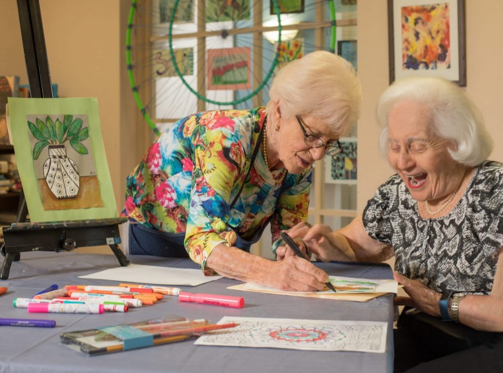 Two senior women enjoying a creative painting session together.