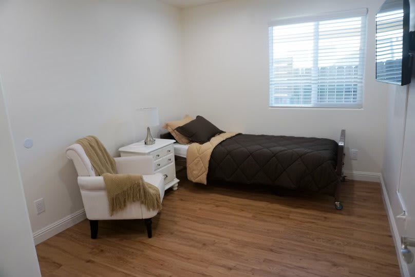 A minimalist bedroom with a single bed, nightstand, and chair on a wooden floor.