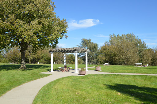 A serene park setting featuring a white pavilion surrounded by lush green grass and trees under a clear blue sky.