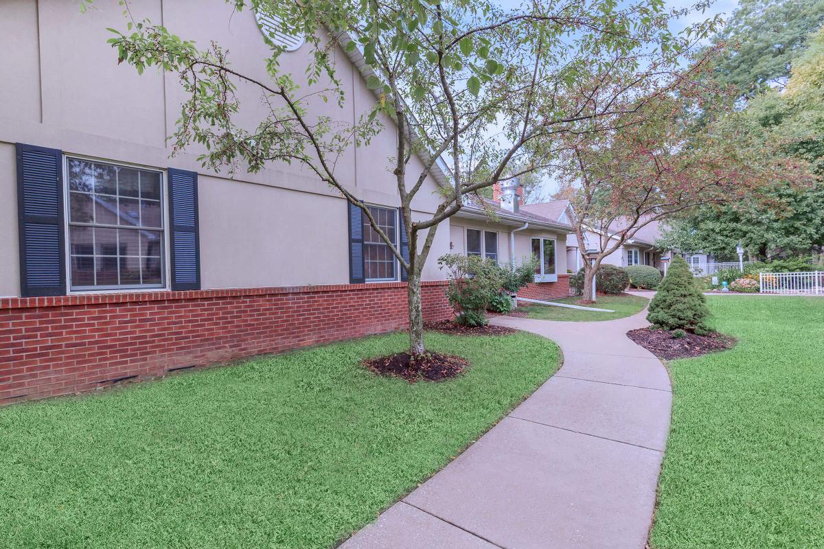 A curved concrete pathway leading to a house, surrounded by well-maintained lawns and trees.