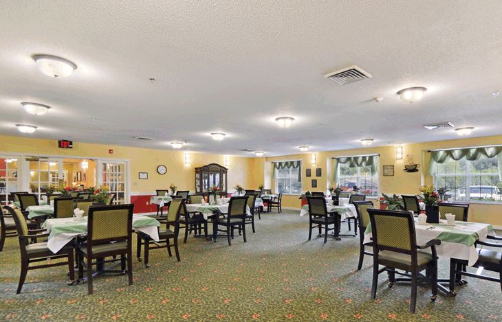 A spacious dining room with neatly arranged tables and chairs, featuring large windows and soft lighting.