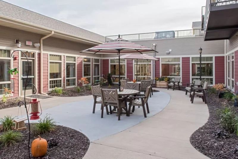 An outdoor patio area with tables, chairs, and umbrellas set in a courtyard surrounded by a building.