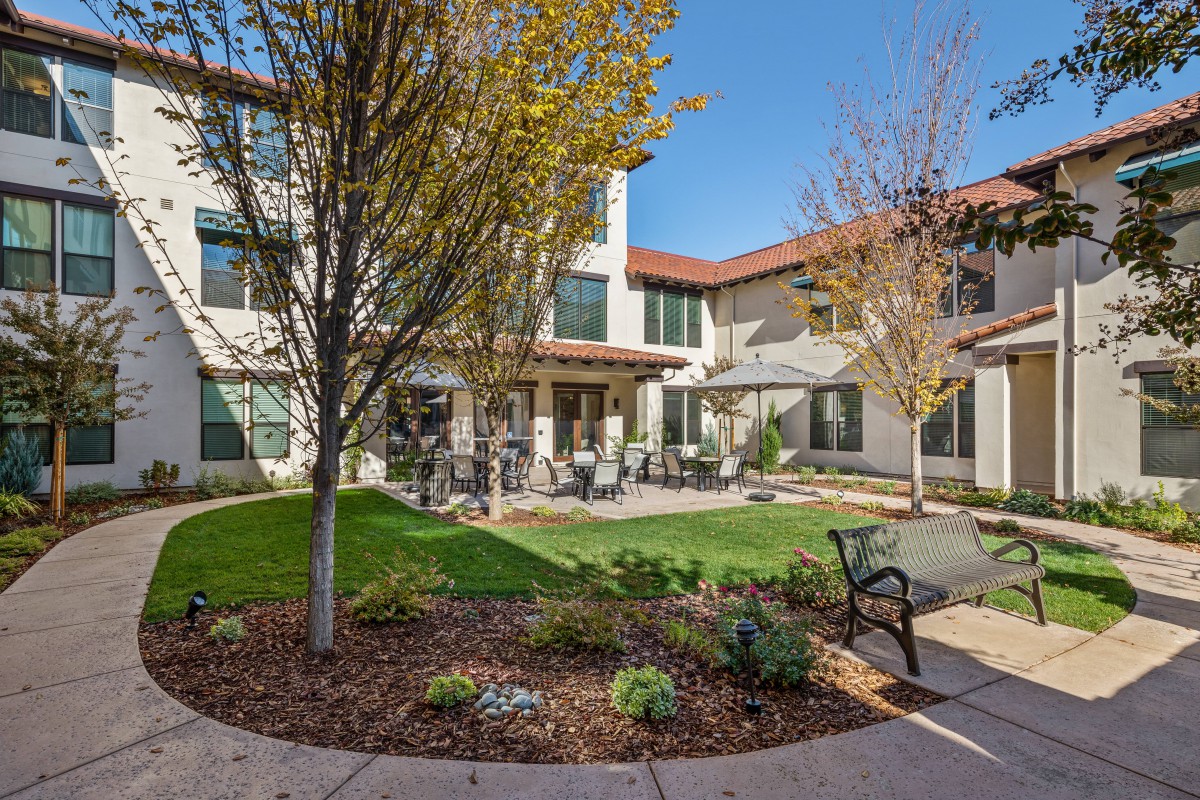 A peaceful courtyard with seating and landscaping in front of a two-story building.
