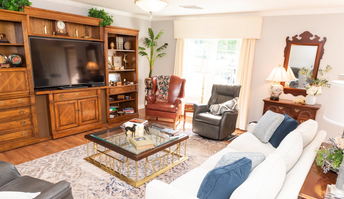 A cozy living room with a sofa, two chairs, a coffee table, and a large television in a wooden entertainment center.