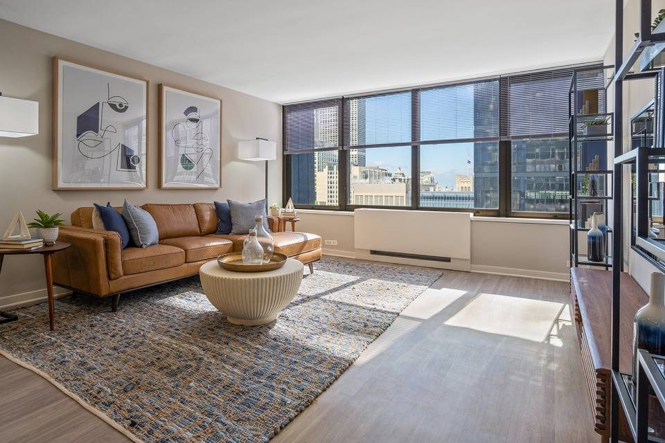 A modern living room with large windows offering a city view, featuring stylish furniture and contemporary decor.