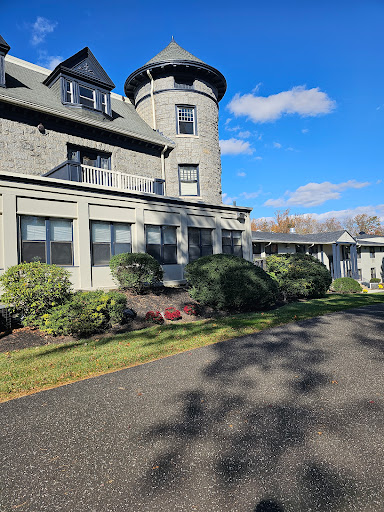 A majestic historic mansion with a tower, surrounded by a well-kept garden under a clear blue sky.
