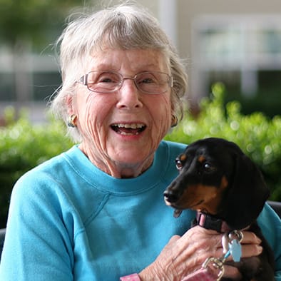 An elderly woman smiling while holding her dog outside.
