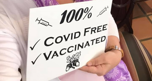 A sign indicating that the individual is 100% COVID free and vaccinated.