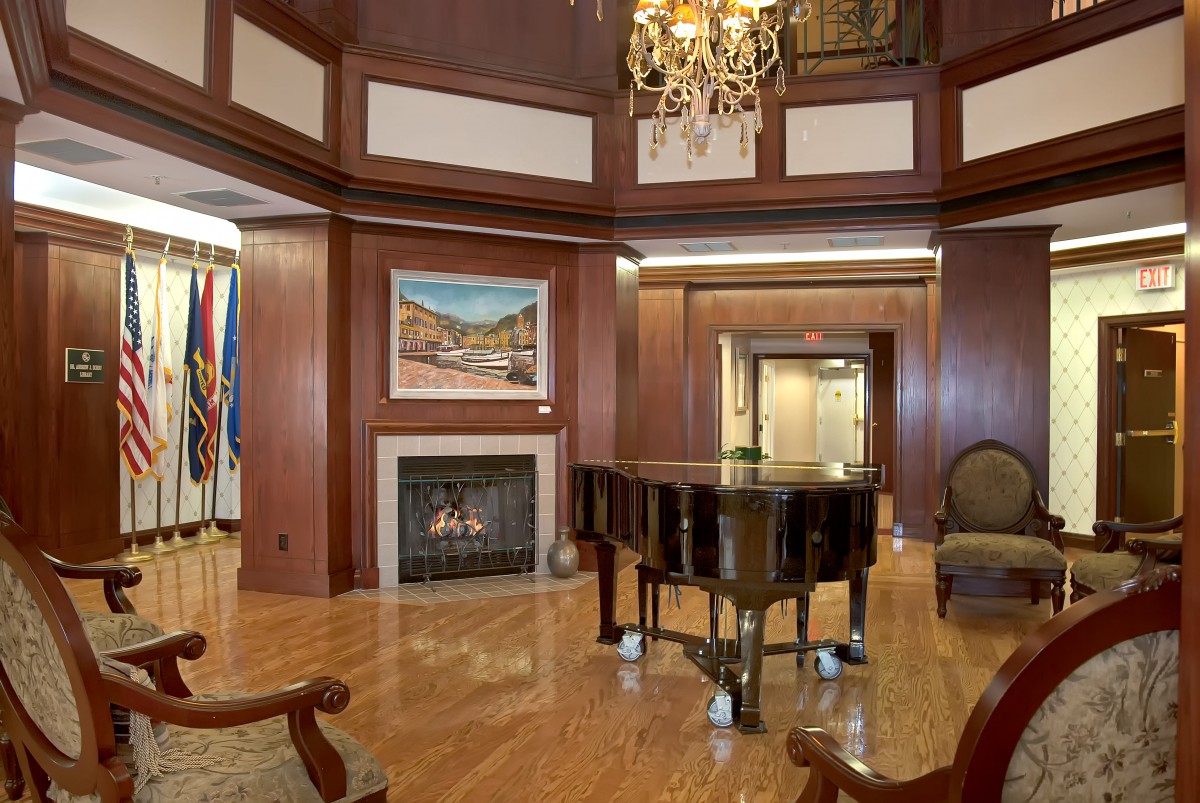 Elegant room featuring a grand piano and a cozy fireplace with wood paneling and a chandelier.