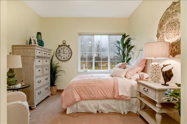 A cozy bedroom with pastel tones, featuring a bed, dresser, and potted plants by the window.