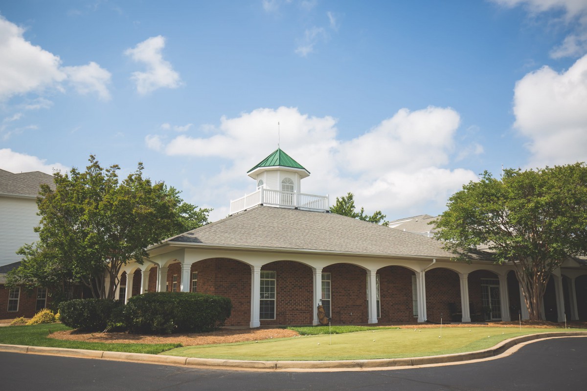 A brick building with a green-roofed cupola surrounded by trees under a blue sky.