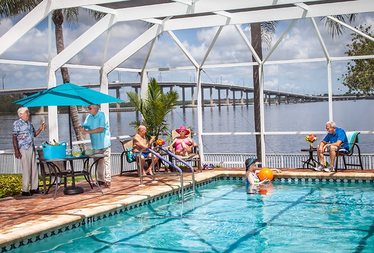 A family enjoying a sunny day by the pool with a scenic view of the bridge and water in the background.