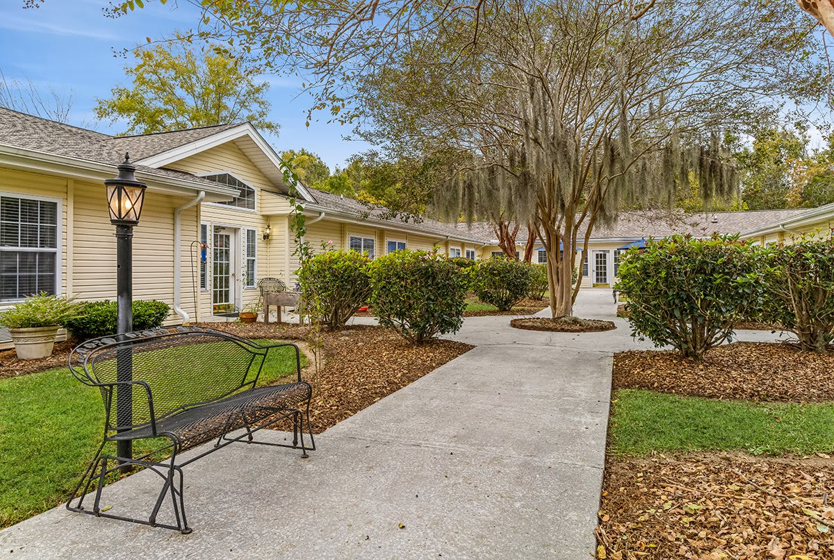 A serene outdoor pathway lined with greenery and benches leading to a building.