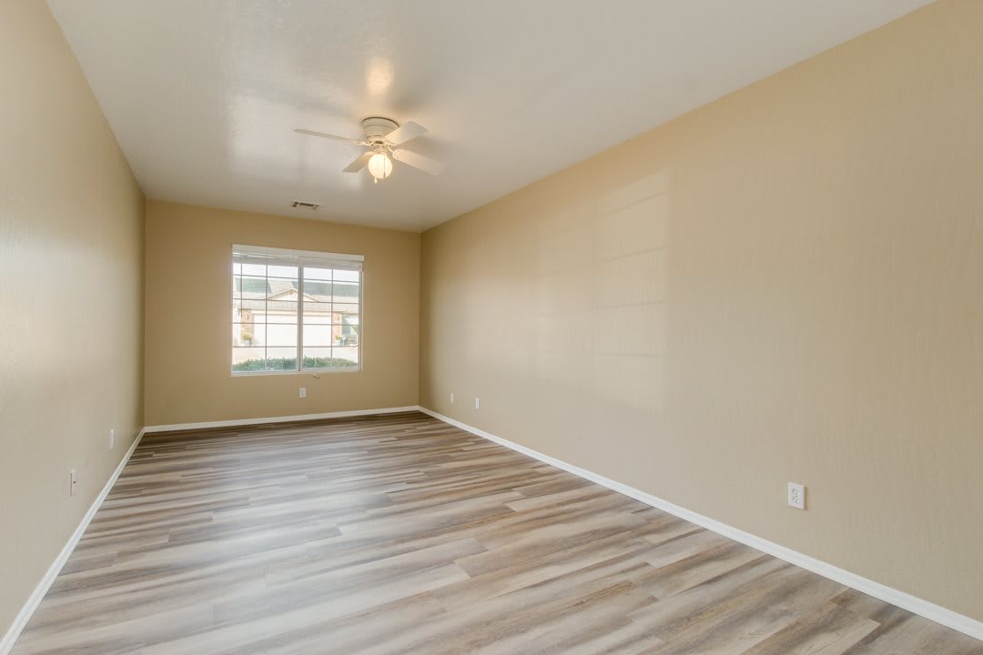 An empty room with wood flooring, featuring a window and ceiling fan.