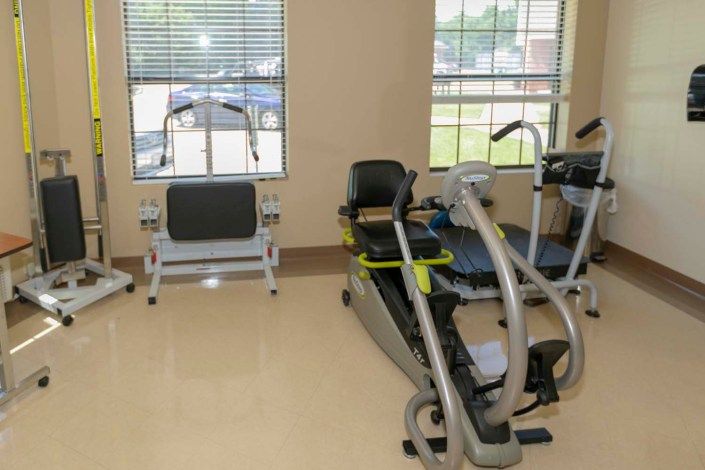 A gym room with various exercise equipment and natural light from windows.