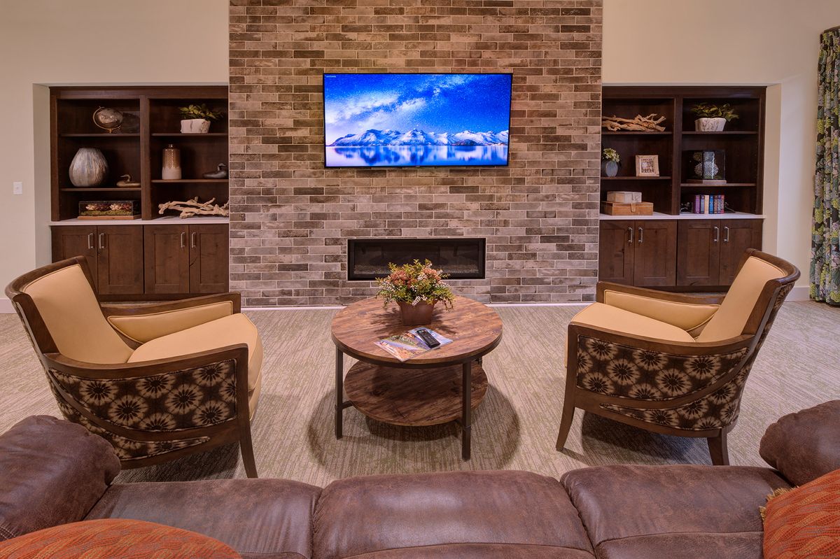 A modern living room with a brick accent wall, featuring a mounted TV, fireplace, and comfortable seating.