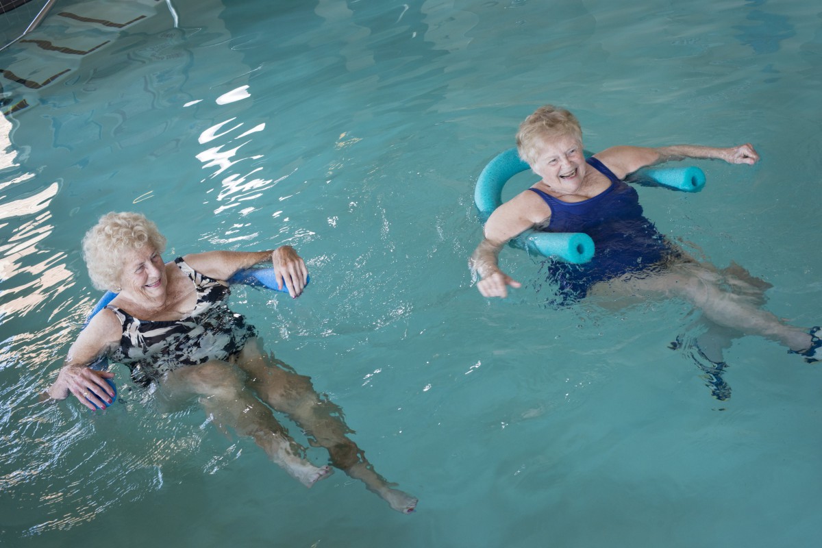 Two seniors enjoying water exercises in a swimming pool.