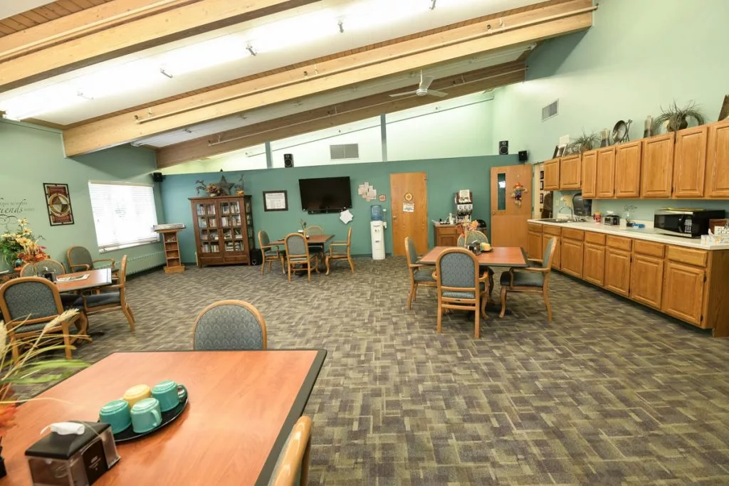 A spacious community room featuring several tables and chairs, a television, and cabinetry.