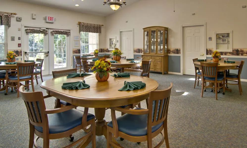 A cozy dining room with wooden tables and chairs, adorned with floral centerpieces and natural lighting.