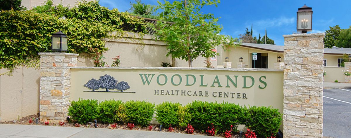 Entrance sign for Woodland Healthcare Center with surrounding greenery.