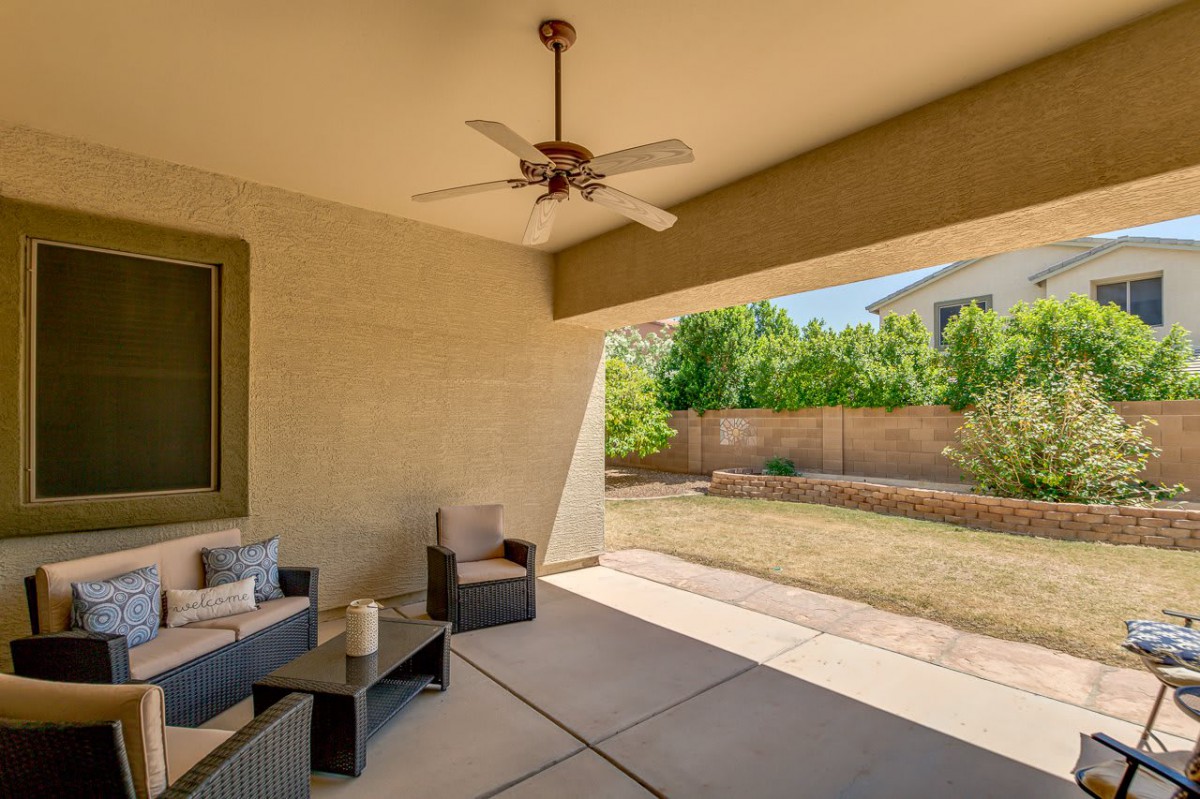 An outdoor patio with seating and a ceiling fan overlooks a backyard.