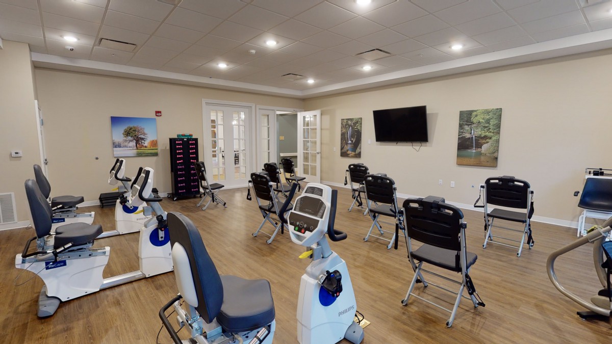 A spacious exercise room with various gym equipment and chairs arranged around a central area.