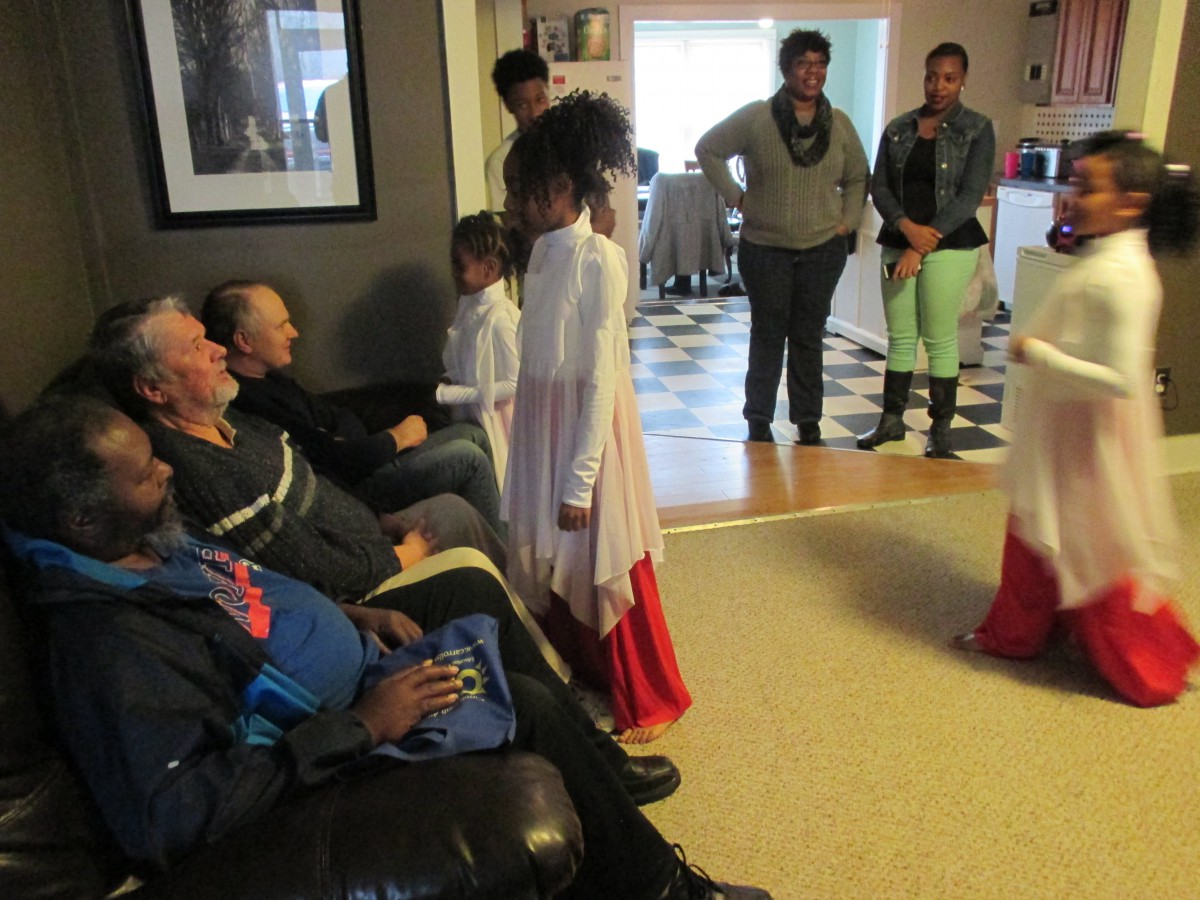 A family gathering with children in white and red outfits performing for seated adults.
