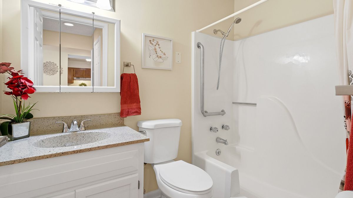 A clean and modern bathroom with a white toilet, sink, and shower equipped with a grab bar, accompanied by a red towel hanging on the wall.