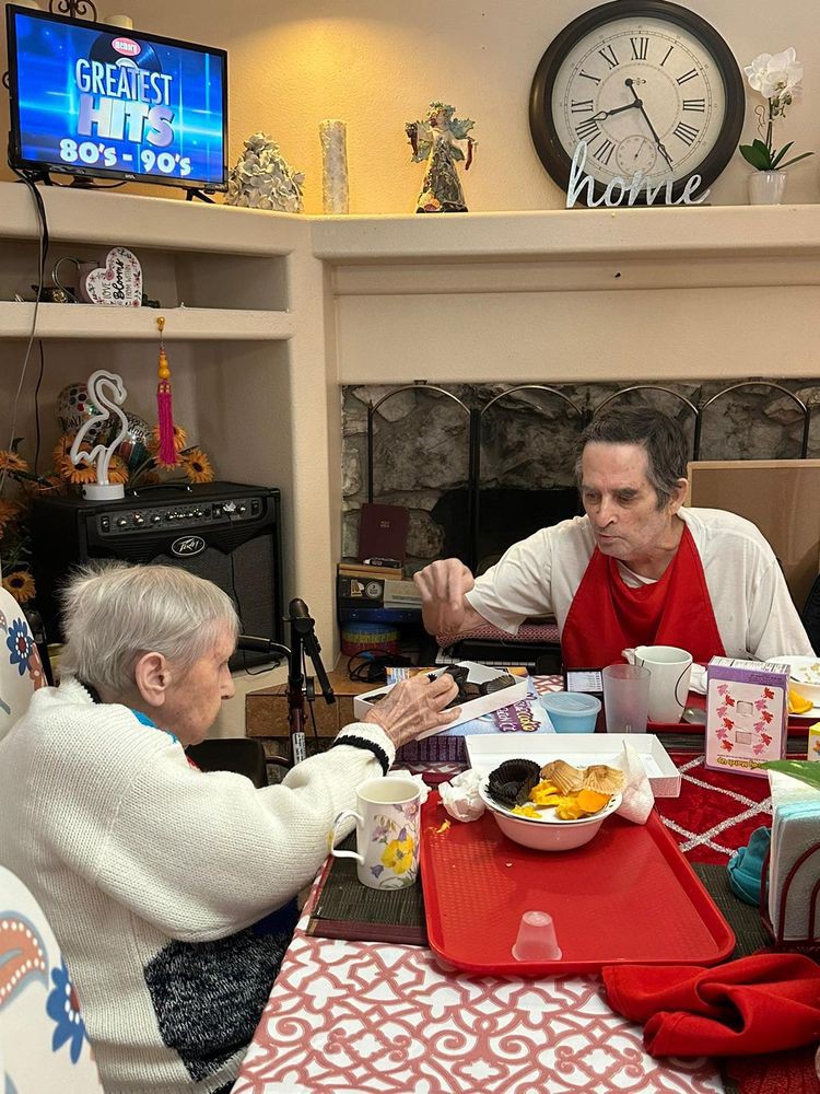 Two elderly individuals sharing a meal together at a dining table in a cozy indoor setting.