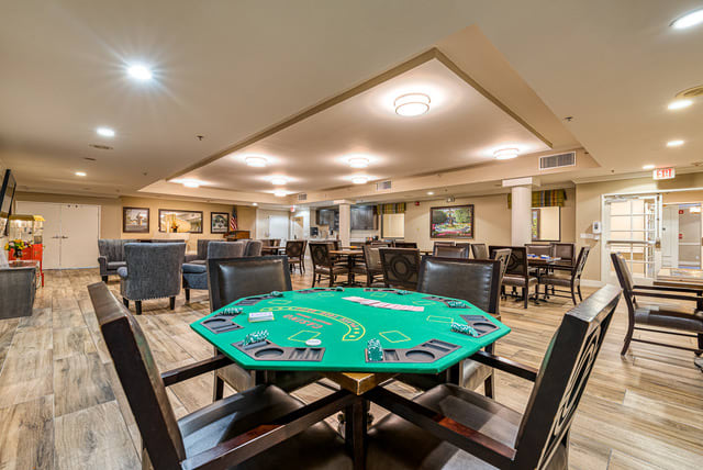 A casino gaming room featuring a poker table with green felt and surrounding seating.
