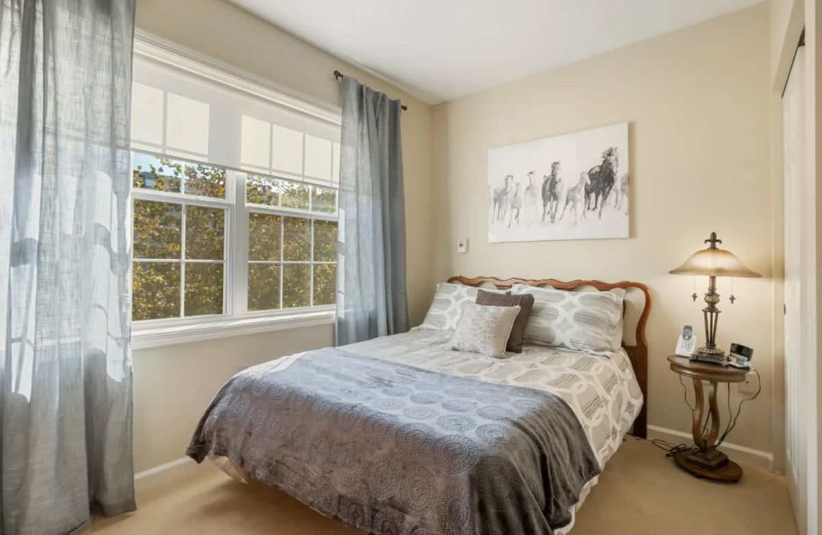 A cozy bedroom featuring a neatly made bed, soft curtains, and a decorative painting on the wall.