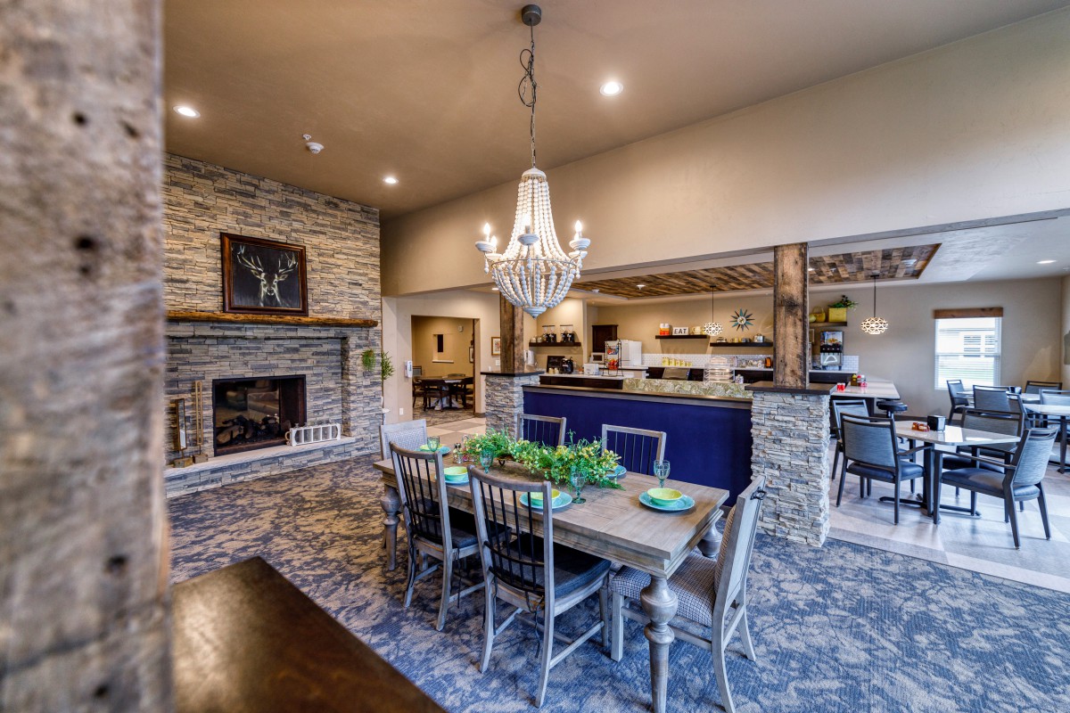 A stylish dining area with a rustic stone fireplace and an open kitchen featuring a chandelier and elegant decor.