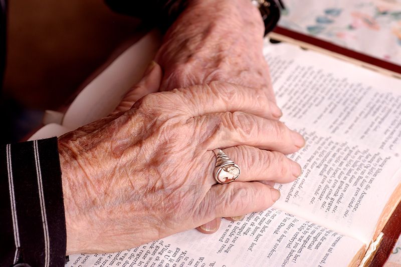 An elderly person with their hands resting on an open book, adorned with a ring.