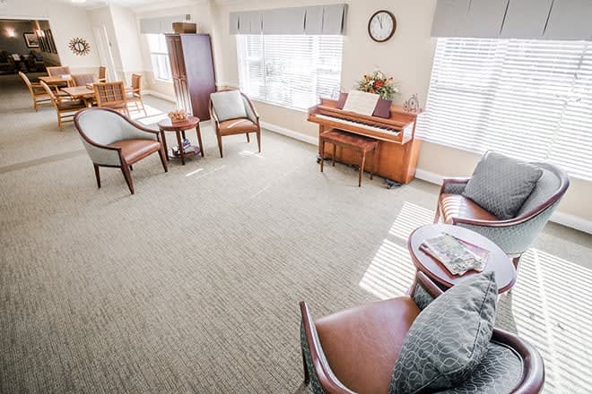 A bright living room with a piano, chairs, and large windows.