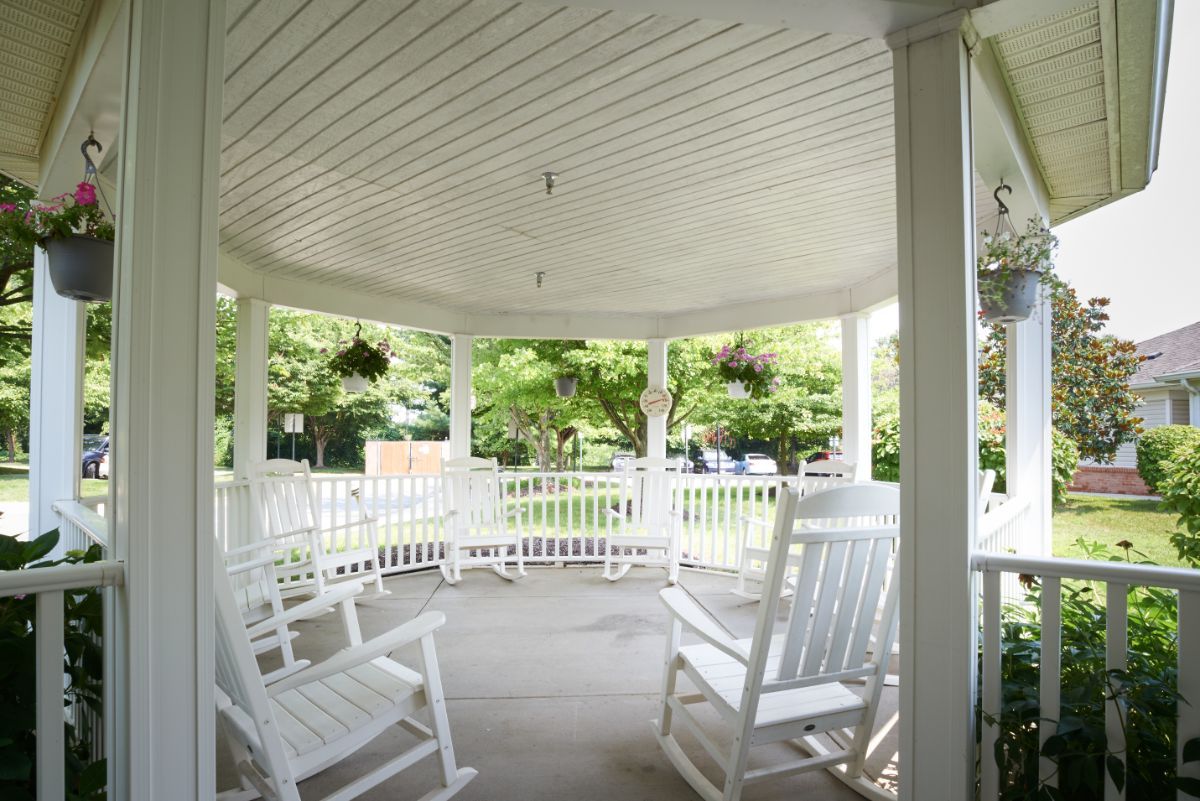 A peaceful gazebo with white rocking chairs overlooking a lush garden.