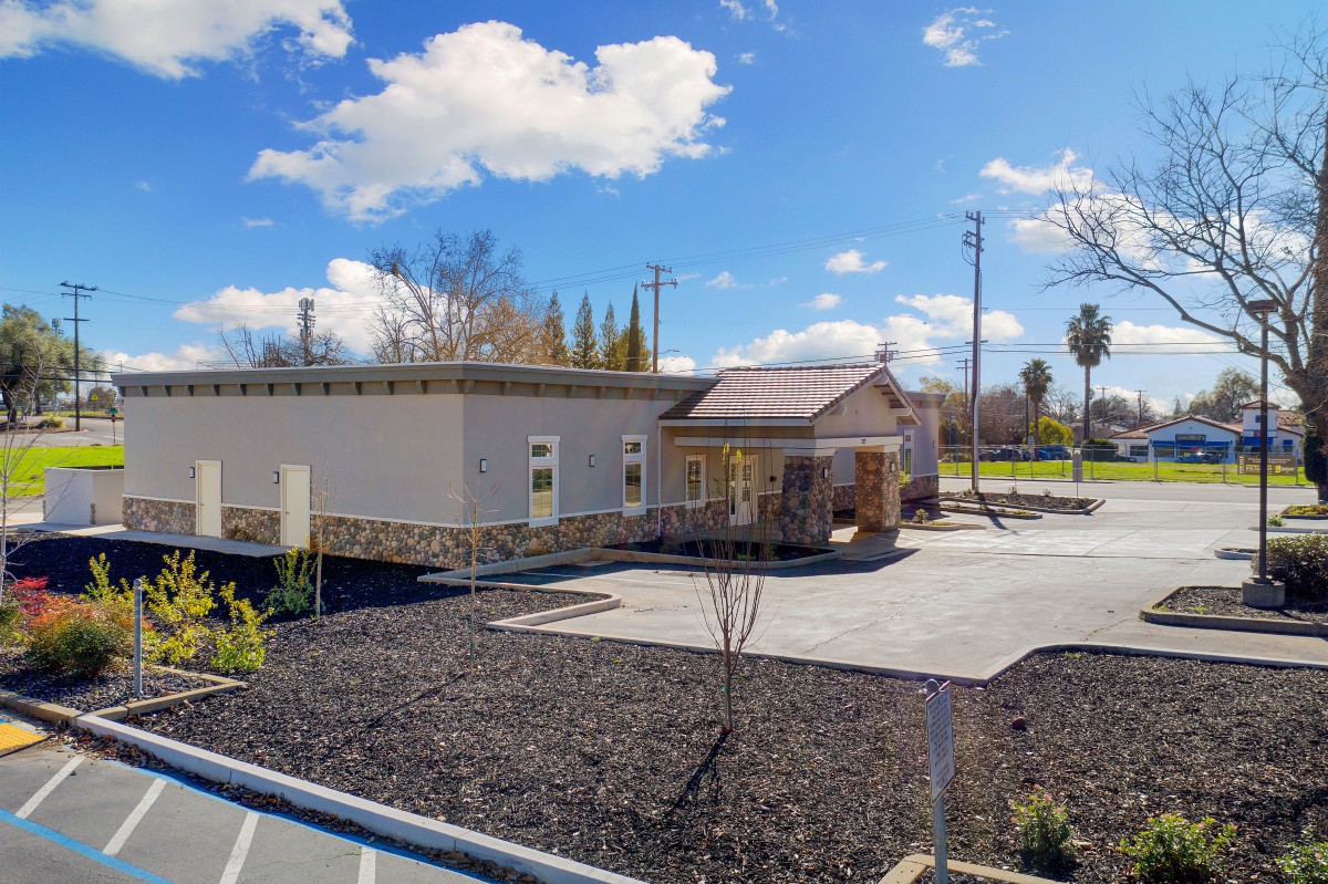 A small building with a parking lot and minimal landscaping under a clear, sunny sky.