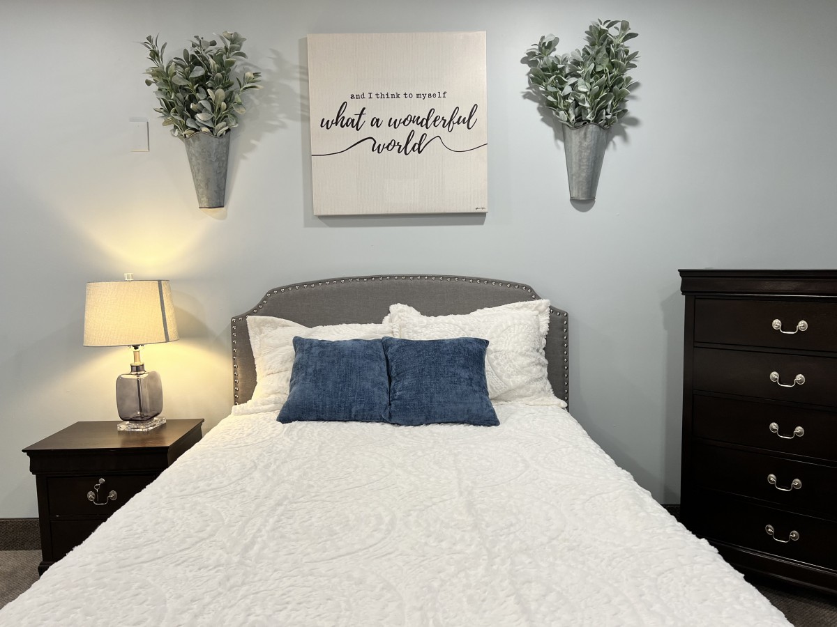 A cozy bedroom with a neatly made bed, decorative pillows, wall art, and plants.